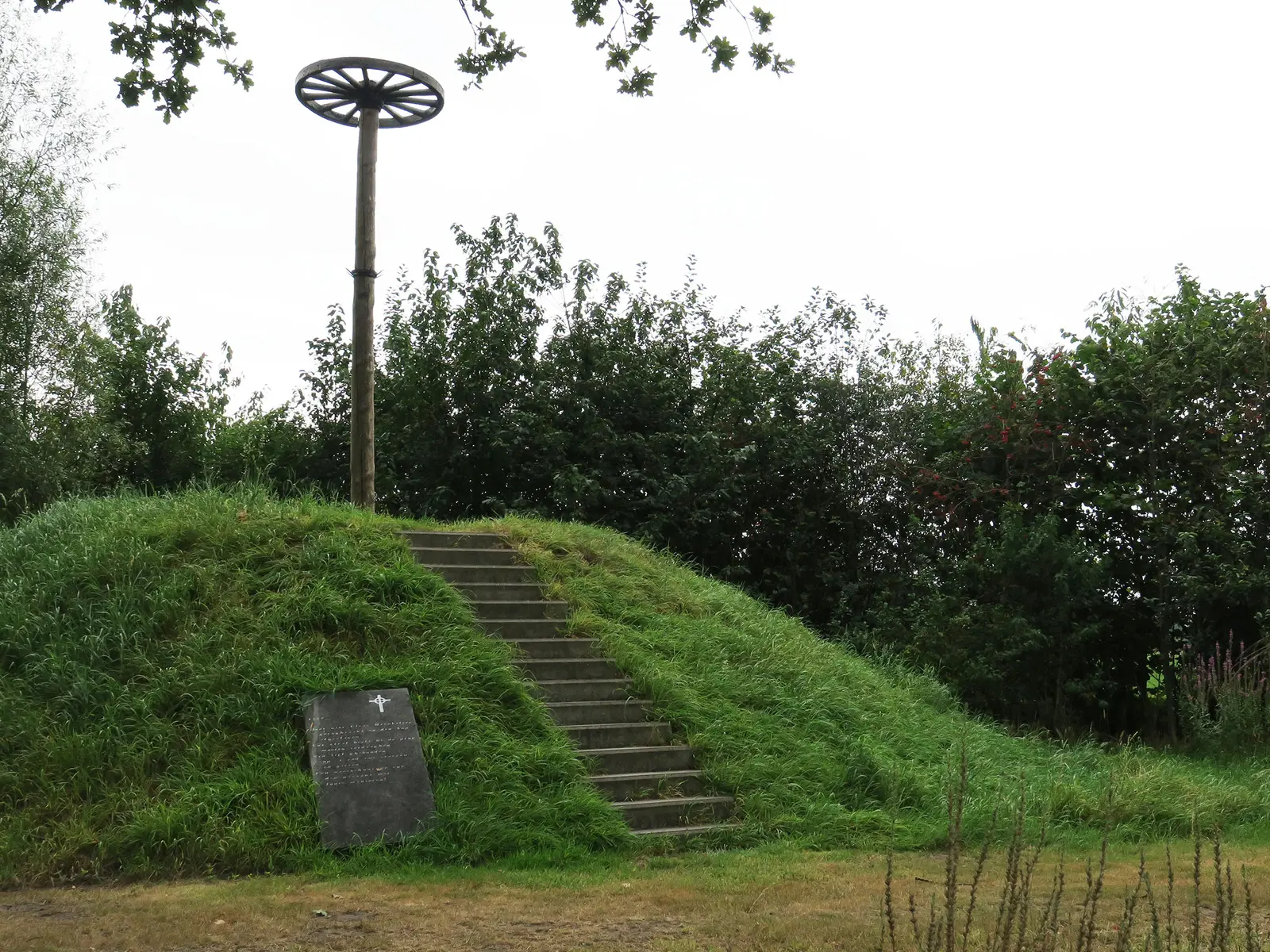 Met gras begroeide heuvel met een houten wiel op een paal
